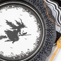 Close up angled view of the vintage witch dessert plate layered directly over an intricate black lace scalloped paper charger.