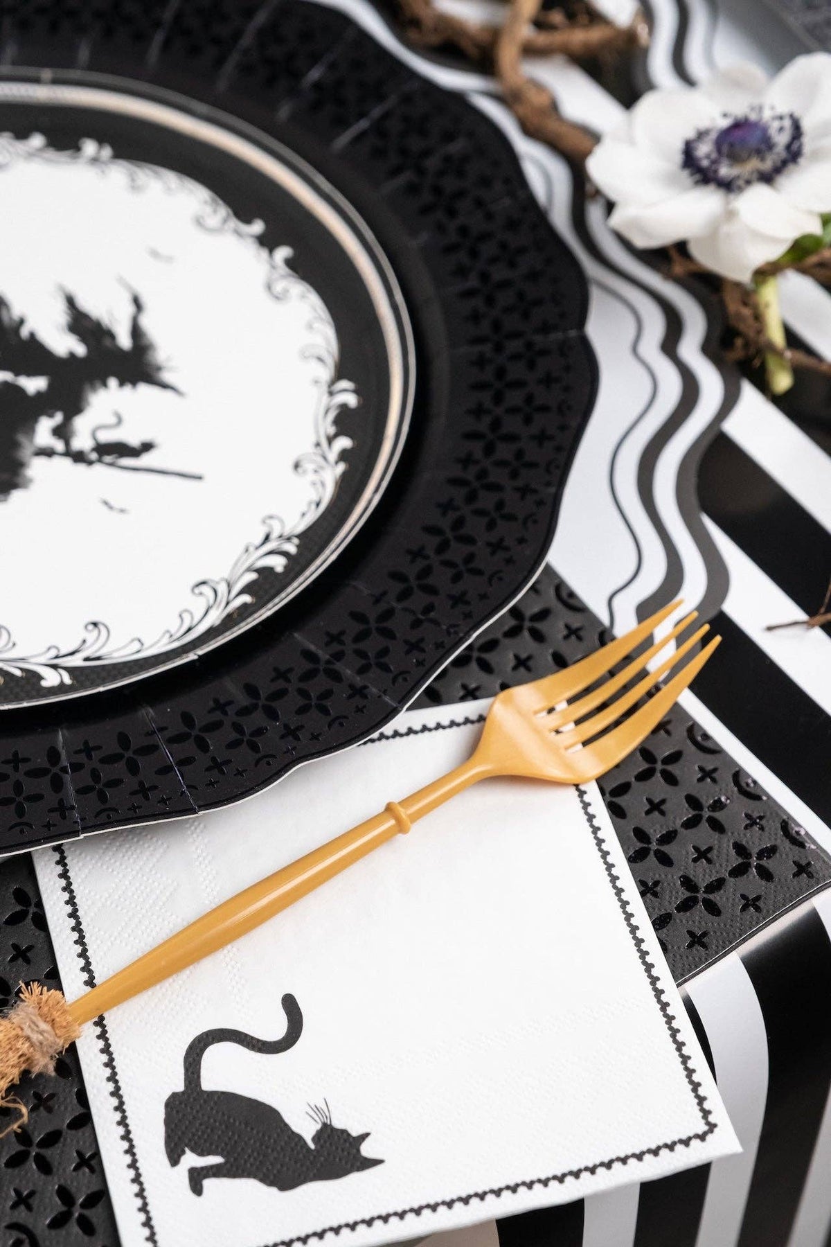 Close up angled view of a vintage witch plate and a black cat paper napkin tucked neatly under gold flatware on a striped runner.
