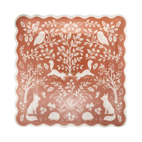 Angled view of the woodland folk-art plate showing the symmetrical deer, bird, and botanical illustration and cream wavy edge detail.