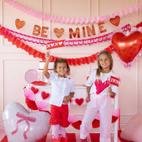 Children holding XOXO felt pennants in a Valentine-themed party setup